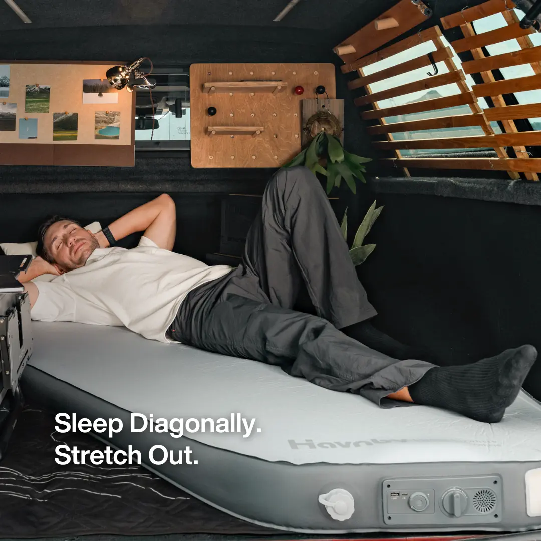 Man lying diagonally across the Havnby CloudCore Diagonal mattress inside a vehicle bed conversion, demonstrating the diagonal sleeping layout