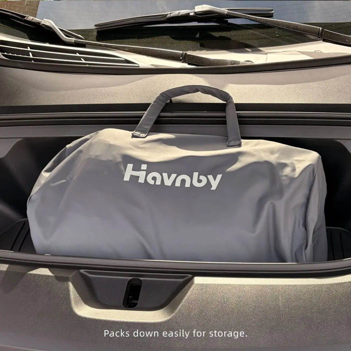 Gray Havnby-branded storage duffel bag positioned in a vehicle cargo area, with on-image text reading Packs down easily for storage
