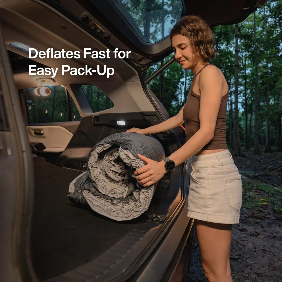 A hand rolling the deflated Havnby CloudCore Seamless Support Mattress for SUV into a bundle inside an SUV cargo area