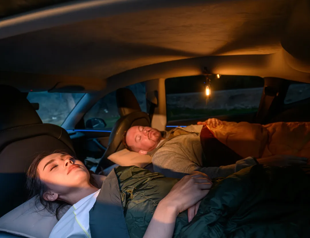 Two people asleep in sleeping bags on a Havnby CloudCore mattress in a Tesla Model Y at night