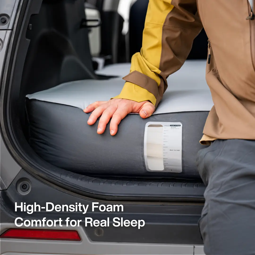 A hand pressing on the Havnby FlatCore mattress at the open tailgate, beside a bilingual thickness-reference sticker with centimeter and inch markings