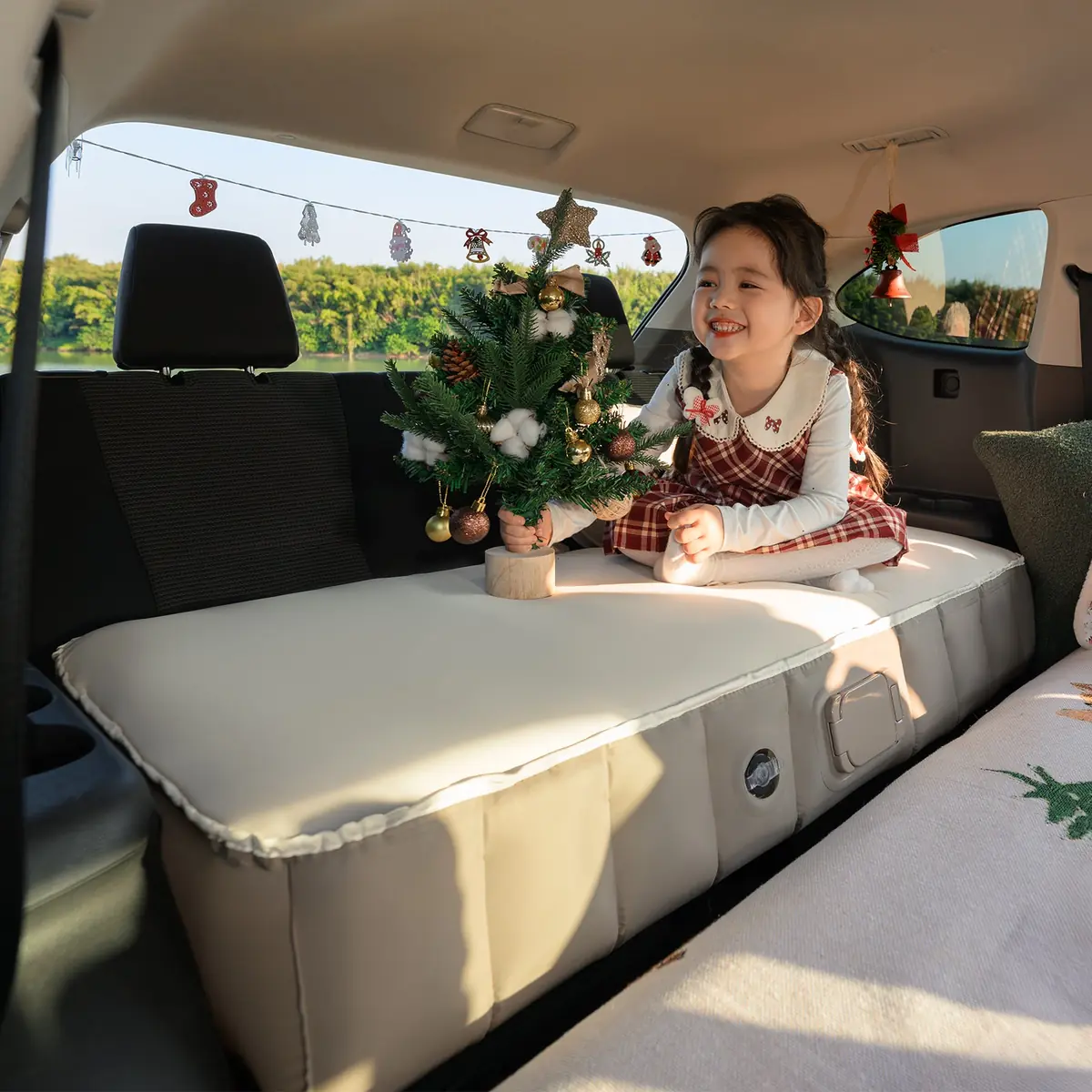Child sitting on the Havnby MiniNest pad in a Toyota Highlander third row with a small decorated tree