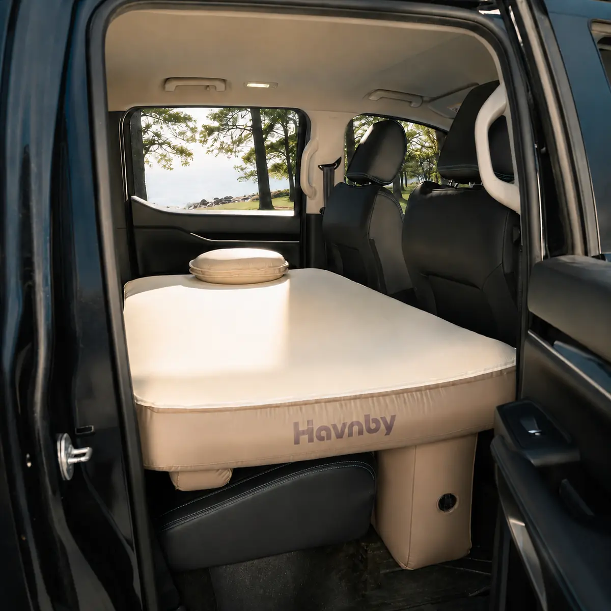 Havnby SnugNest pad installed across the rear seat and footwell of a mid-size pickup truck crew cab, with a pillow on top and rear doors open