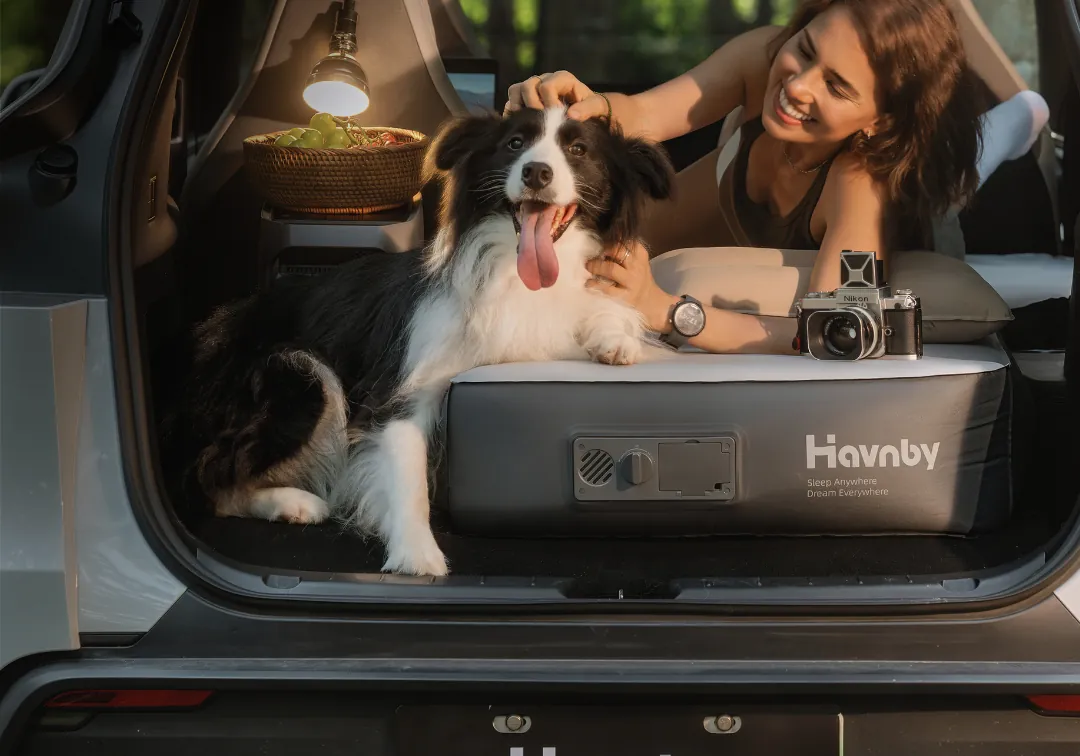 A woman and a border collie on a Havnby FlatCore Solo mattress at the open hatch of a Tesla Model Y L