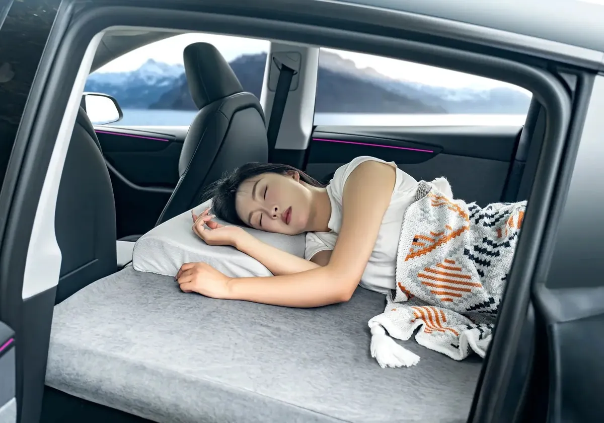 A woman asleep on a NovaPads mattress in a Tesla Model Y, a lake beyond the window